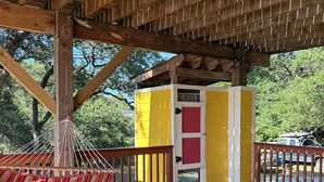 A wooden deck with a hammock, a yellow and red building, and a vehicle in the background.