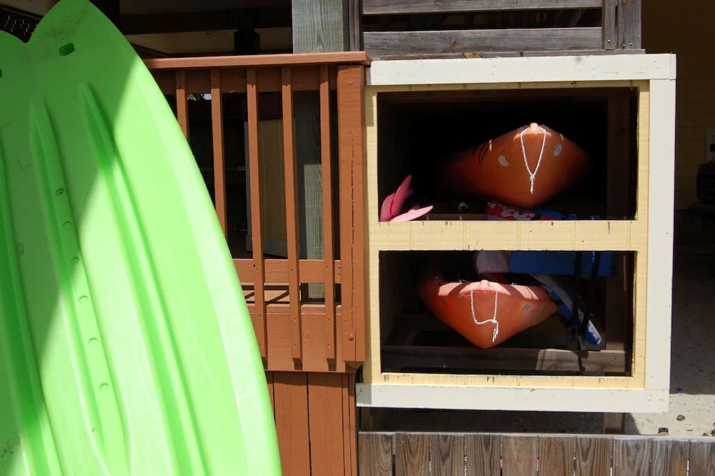 Een houten constructie met twee opbergkisten, waarvan er een een rood voorwerp en de andere een roze voorwerp bevat.