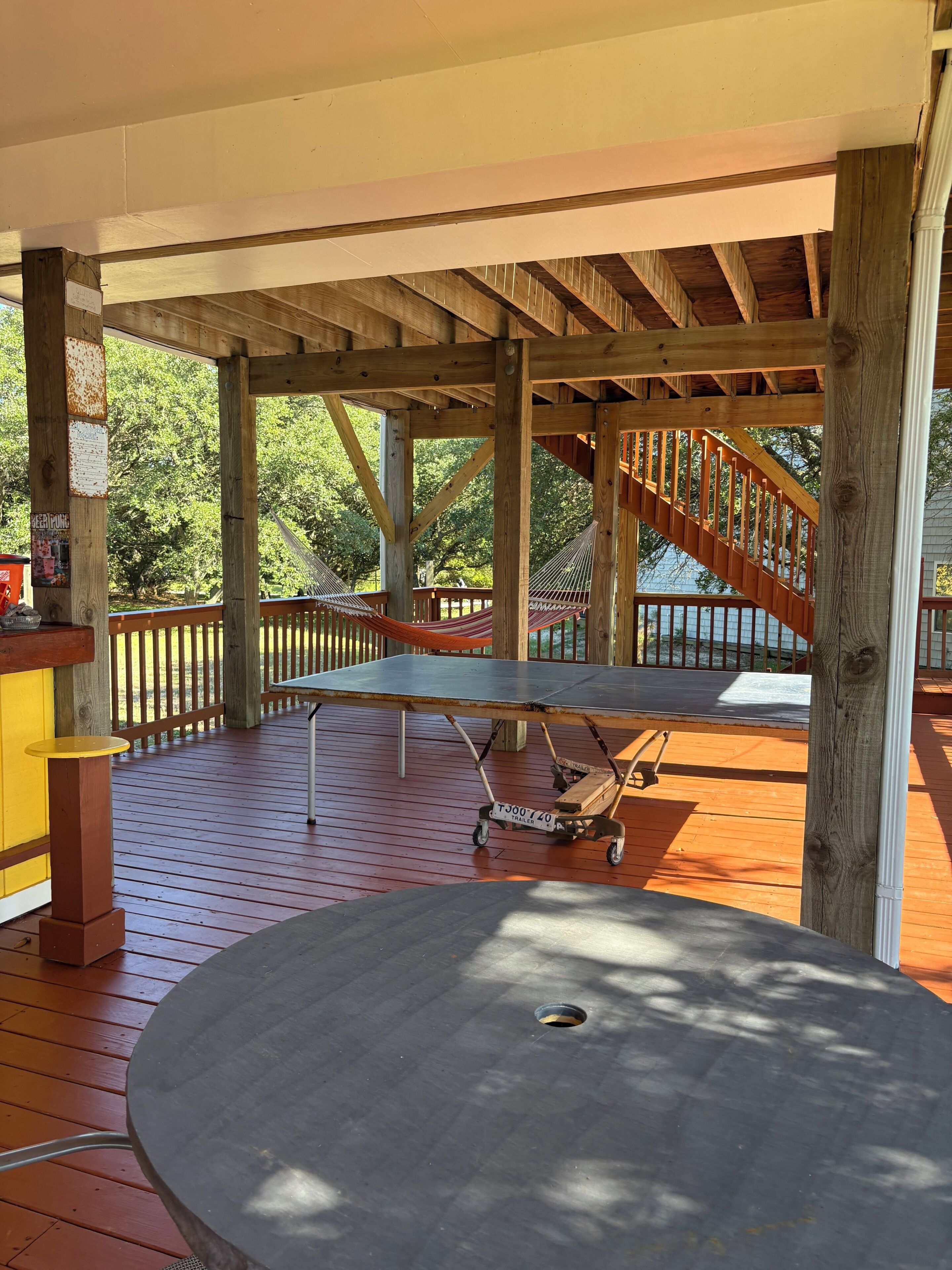 A covered outdoor area with a table, a hammock, and a staircase.