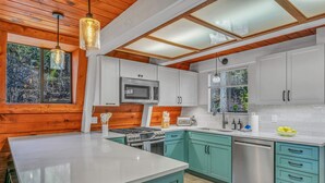 A modern kitchen with white and teal cabinetry, a large island, stainless steel appliances, and a skylight. - Cozy Cabin | Large Deck + Near the Slopes (Homewood)
