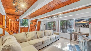 A cozy living room with a wooden ceiling, a beige sofa, and a fireplace. - Cozy Cabin | Large Deck + Near the Slopes (Homewood)