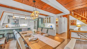 A modern kitchen with white cabinets, a wooden dining table set for six, and a staircase leading to an upper level. - Cozy Cabin | Large Deck + Near the Slopes (Homewood)