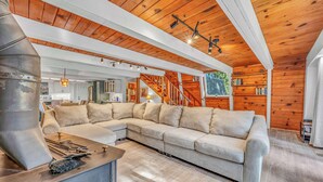 A modern living room with a sectional sofa, a fireplace, and a staircase leading to an upper level. - Cozy Cabin | Large Deck + Near the Slopes (Homewood)