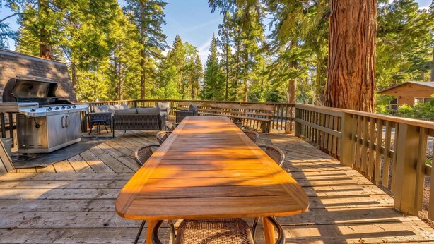 A wooden deck with a grill, seating, and a view of a forest. - Cozy Cabin | Large Deck + Near the Slopes (Homewood)