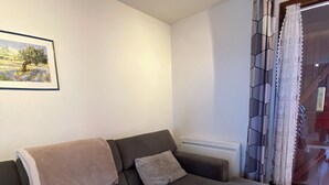 Una sala de estar moderna con un sofá seccional gris oscuro, un radiador blanco, cortinas estampadas y un cuadro con un paisaje en la pared.