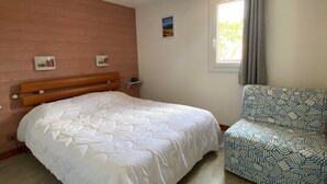 Un dormitorio con cama, una silla, un ventanal y un cuadro colgado en la pared.