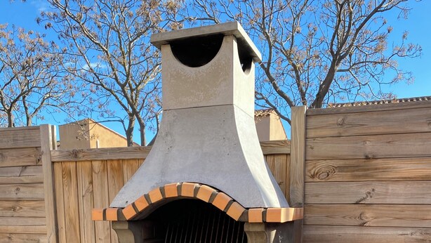 Un horno de ladrillo al aire libre con chimenea, un banco de madera y un pozo de fuego.