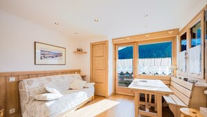 A cozy room with a wooden bed, a small table, and a window with a view of the outdoors. - Le Beauregard 1 - Vue Montagne (Le Grand Bornand)