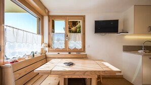 A compact kitchen with wooden furniture, a television, and a window with curtains. - Le Beauregard 1 - Vue Montagne (Le Grand Bornand)