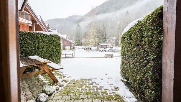 A snowy courtyard with a wooden bench, a paved path, and a view of a mountain range. - Le Cocon des Pistes - Station à 10 minutes (Les Contamines-Montjoie)