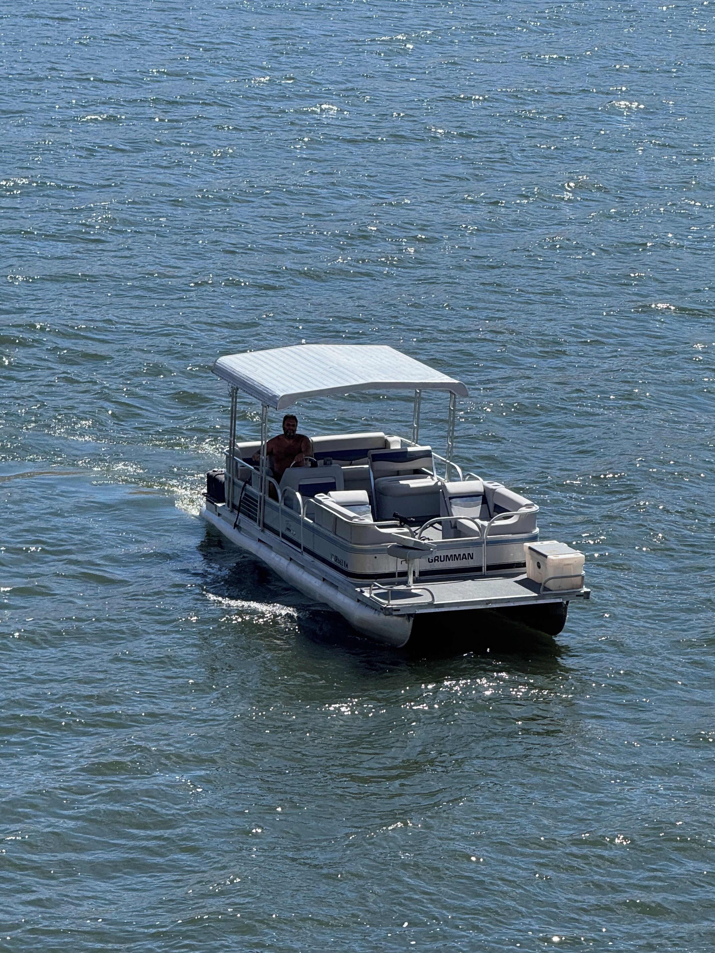 A small motorboat with a canopy, a person seated at the helm, and a wake behind it.