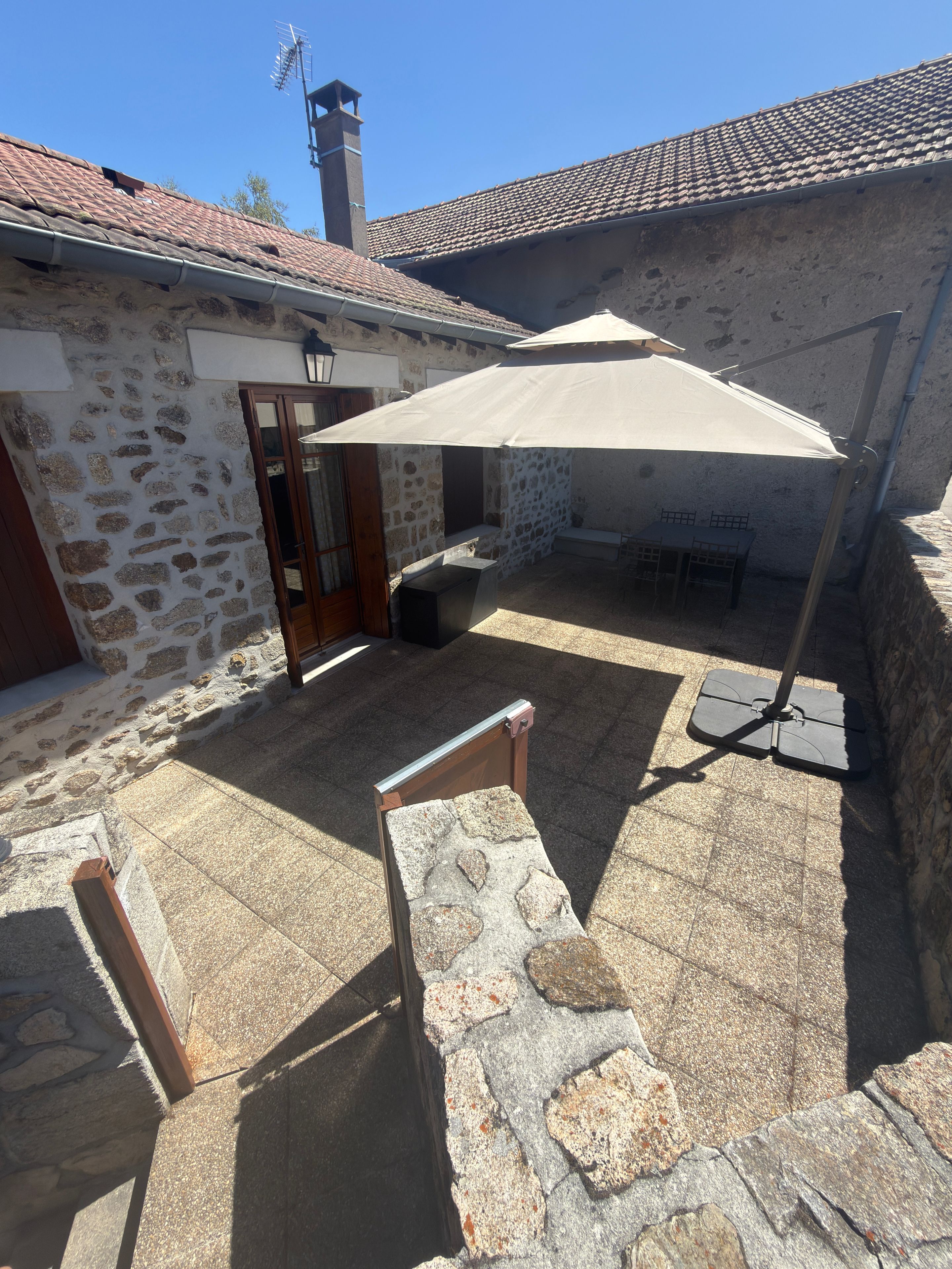 A stone building with a tiled roof, a covered patio area, and a swing set.