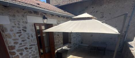 A stone building with a tiled roof, a covered patio area, and a swing set.