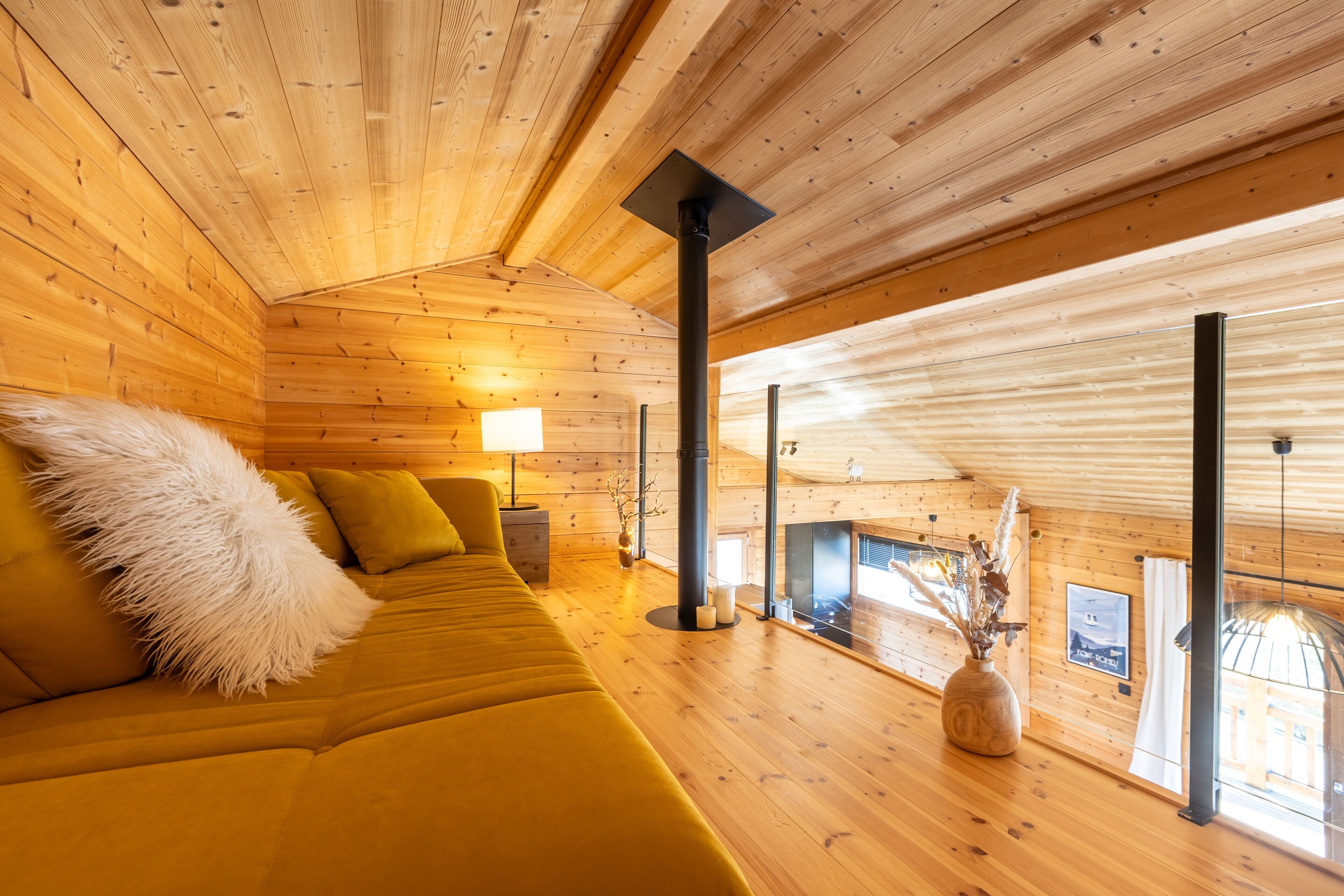 Ein Holzblockhaus-Innenraum mit einer Couch, einer Lampe und Blick durch ein Fenster.