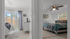 Een slaapkamer met een bed, een plafondventilator, een raam en een deur die leidt naar een balkon.