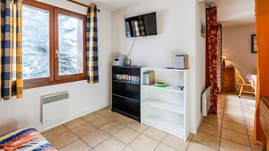 Una habitación con cama, televisor en la pared, estantería y radiador.