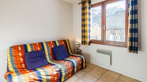 Una habitación con sofá, ventana con cortinas, lámpara y radiador.