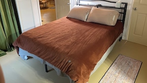 A bed with a brown blanket, a bedside table with a lamp, and a door leading to a room with a chair and a window. - The Jumping Mullet in charming Crystal River, walk to bars, restaurants & bay (Crystal River)