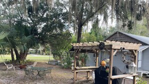 A wooden pergola with a covered seating area, surrounded by trees and a lawn. - The Jumping Mullet in charming Crystal River, walk to bars, restaurants & bay (Crystal River)