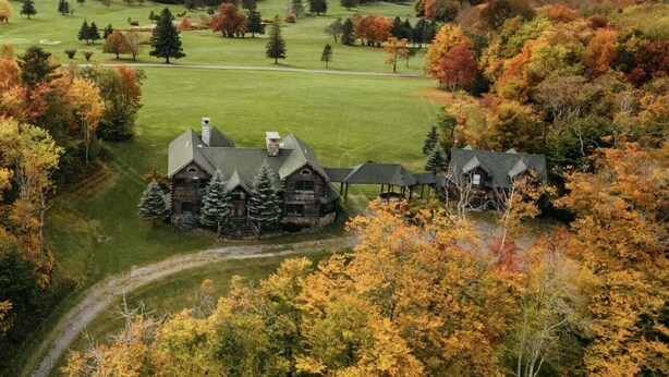 Ein großes, rustikales Lodge-Gebäude mit mehreren Holzhütten und einem gepflegten Rasen, umgeben von Bäumen in Herbstfarben.