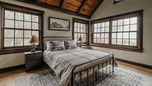 Ein Schlafzimmer mit einem großen Bett, zwei Nachttischen, einer Holzbalkendecke und großen Fenstern.