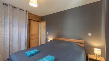 Een slaapkamer met een bed, nachtkastje, lamp, deur en gordijn.