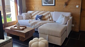 A cozy living room with a wooden wall, a framed picture, a sofa, a coffee table, and a window.