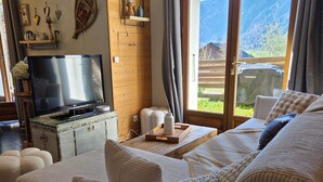A modern living room with a sofa, television, and a view of mountains through large windows.