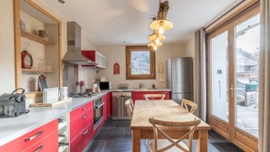 A modern kitchen with red cabinets, a stainless steel refrigerator, and a dining area with a wooden table and chairs.