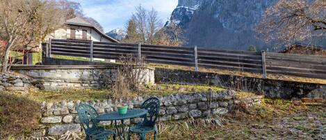 A rustic outdoor seating area with stone walls and metal chairs, overlooking a mountainous landscape.