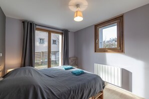 A bedroom with a bed, a window, a radiator, and a view of the outside. - Samoëns – Apartment for 6 with Terrace, Garden & Panoramic Views (Samoëns)
