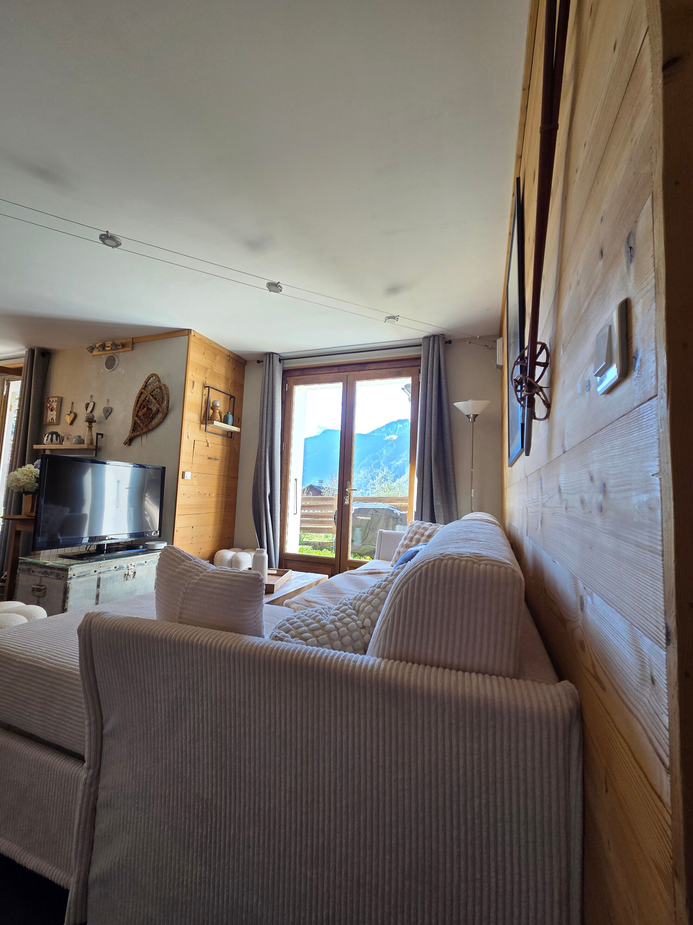 Una habitación con cama, televisión, pared de madera y ventana con vista a la montaña.