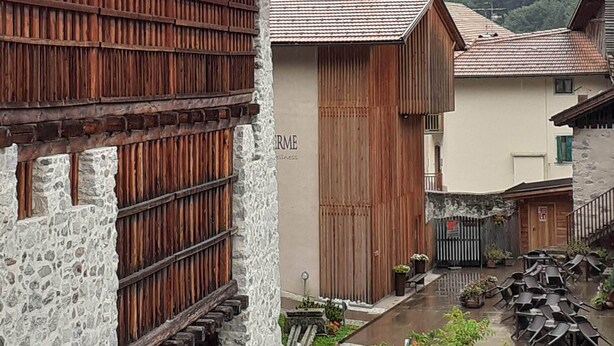 Ein rustikales Gebäude mit Holzhaut und Steinmauern, ein kleiner Garten mit Blumen und eine Bergkulisse im Hintergrund.