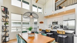 Una cocina moderna con armarios blancos, electrodomésticos de acero inoxidable y un comedor con mesa de madera y sillas tapizadas en verde.