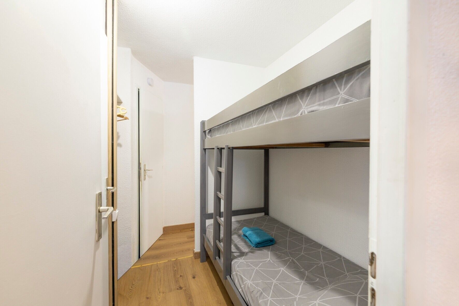 A narrow hallway leading to a bunk bed room with a wooden floor and white walls.