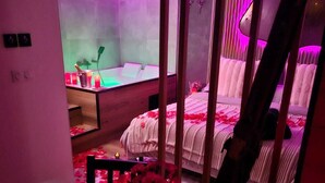 A modern bedroom with a bed, bedside table, and a small seating area. - L'Écrin des Alpes - Romantic Suite with Jacuzzi - Centre Saint-Étienne (Saint-Étienne)