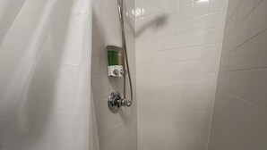 Un baño pequeño con revestimiento blanco de azulejos, un cabezal de ducha de mano y un panel de control.