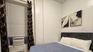 Un dormitorio con cama, un radiador, una ventana con cortinas y dos obras de arte colgadas en la pared.