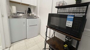 Una cocina compacta equipada con microondas, un lavamanos pequeño y una cafetera sobre una despensa móvil.
