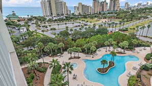 A resort with a large pool, palm trees, and a view of the ocean. - 🏖️Beautiful Views-Lagoon Pool-Hot Tub-Walk2Beach-Luau II- By the Sea☀️ (Miramar Beach)