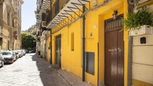 Un carrer estret amb edificis grocs, cotxes estacionats i una porta amb un rètol.
