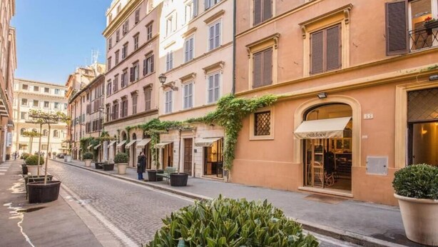 Una calle con edificios, mesas al aire libre y macetas con plantas.