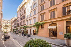 Una calle con edificios, mesas al aire libre y macetas con plantas.