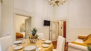 Un área de comedor con una mesa preparada para cuatro, un televisor montado en la pared y un sofá con cojines mostaza.