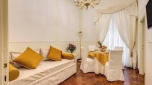 Una habitación con un sofá blanco, cojines amarillos, una araña y una mesa con mantel blanco.