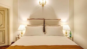 Una cama bien tendida con sábanas blancas, dos lámparas de noche y un candelabro encima.
