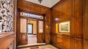 Un pasillo de madera con una puerta que da a una habitación, un cuadro enmarcado en la pared y un revestimiento texturizado a la izquierda.