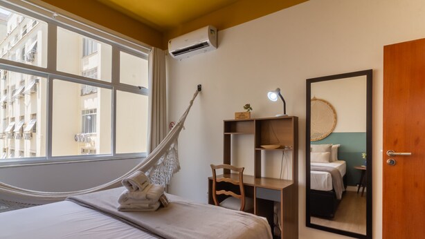 Une chambre à coucher avec un lit, un hamac, un bureau, une chaise, un miroir et une porte.