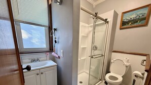 A bathroom with a glass shower enclosure, a toilet, and a sink with a window above. - Western-Themed & Conveniently-Located Apartment in Tonawanda (Tonawanda)