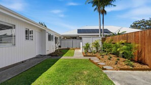 A modern house with a well-maintained lawn, a wooden fence, and a solar panel array. - The Little Husky by Experience Jervis Bay (Huskisson)